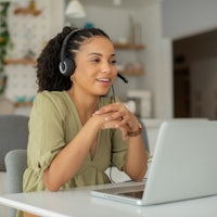 a woman wearing a headset and sitting at a desk with a laptop