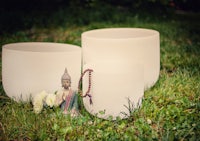 three white bowls with a buddha statue in the grass